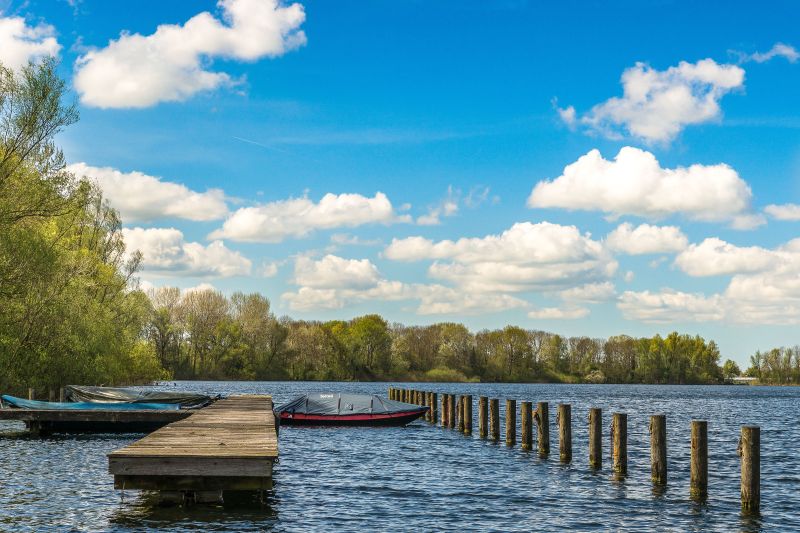 sea-witha-boatas-near-dock-green-trees-distance-blue-sky
